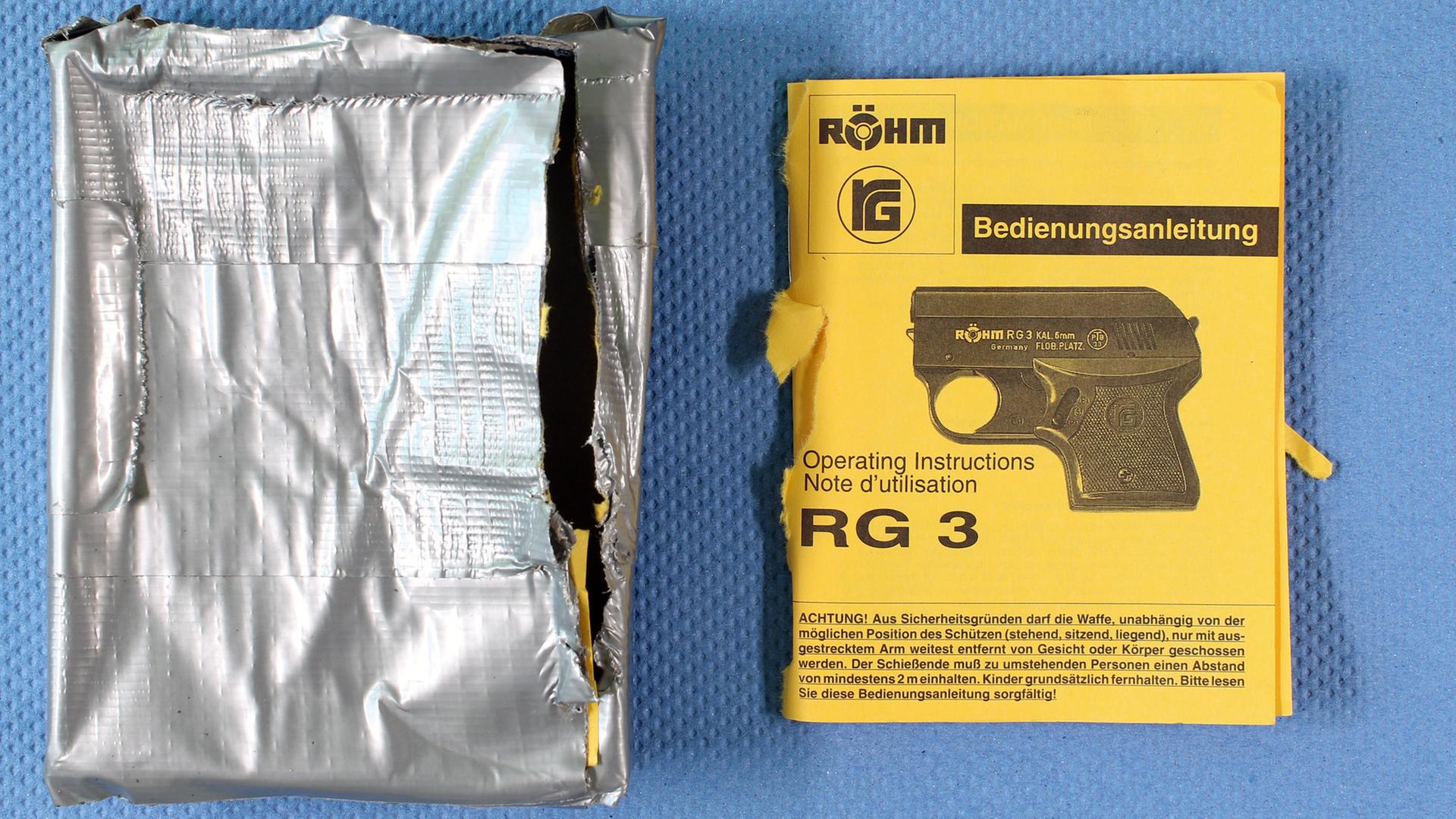 Die Verpackung und Bedienungsanleitung einer Schreckschusswaffe Röhm RG3. Die Verpackung wurde mit Klebeband umwickelt.