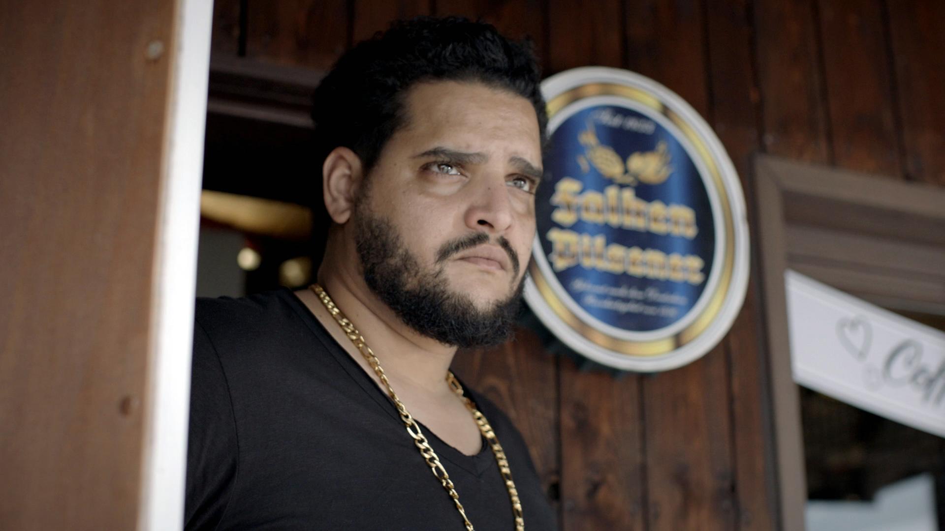 Nachgestellte Szene: Ein Mann steht vor der Tür eines Hinterausgangs und schaut fokussiert in die Ferne