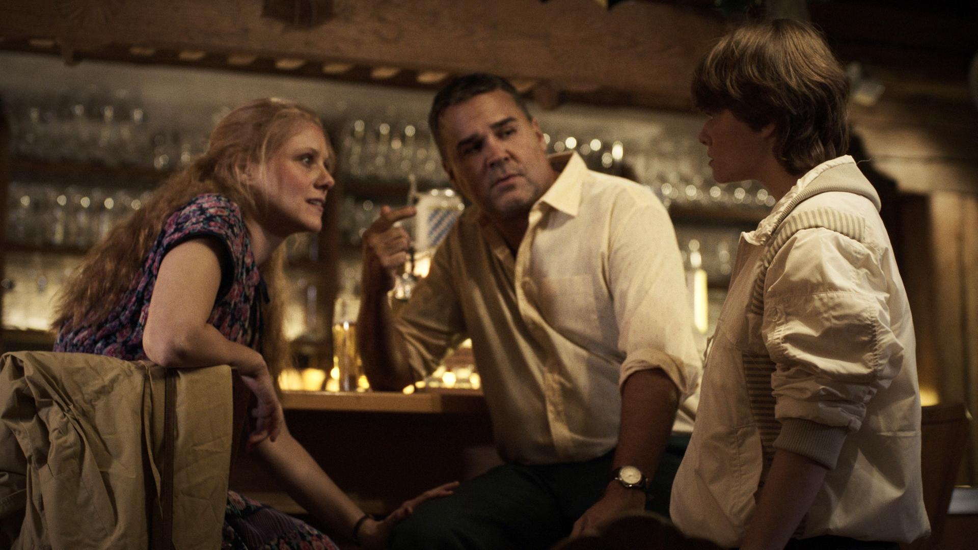 Nachgestellte Szene: Ein Mädchen spricht mit einer Frau, die mit einem Mann an einer Theke sitzt.