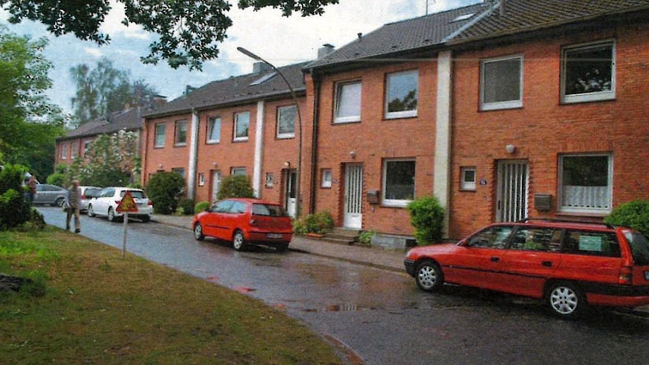 Mehrere Reihenhäuser mit Backstein-Fassade. Auf der Straße vor den Häusern stehen Autos.
