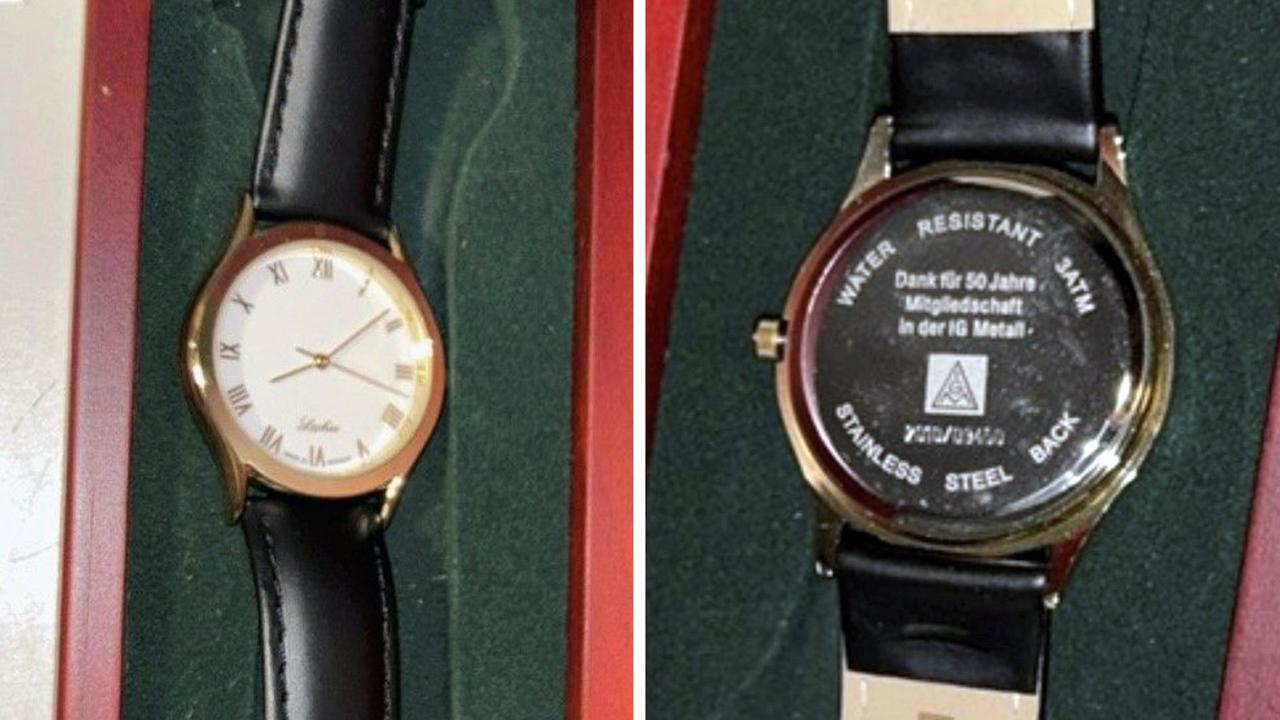 Vorder- und Rückseite einer Armbanduhr mit schwarzem Band, goldener Lünette und weißem Ziffernblatt in einer roten Box mit grünem Futter.