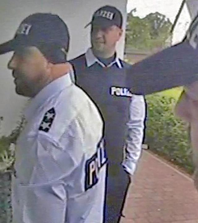 Drei Männer stehen in Polizei-Verkleidung vor einer Haustür.