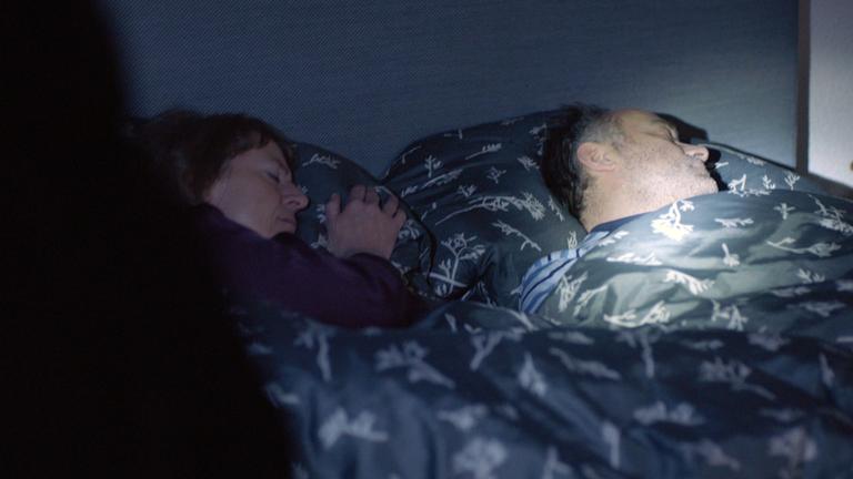 Nachgestellte Szene: Ein schlafendes Ehepaar wird von einer Taschenlampe angeleuchtet, als die Täter in das Haus eindringen.