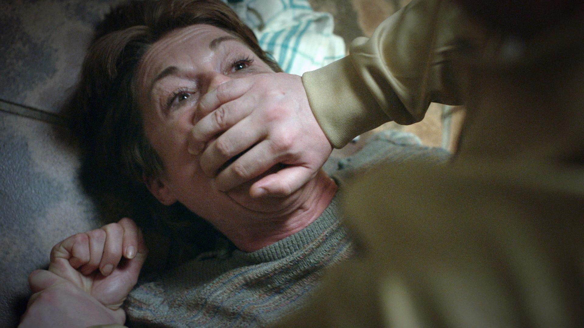 Nachgestellte Szene: Ein Mann überwältigt eine Frau. Er hält ihr mit seiner Hand den Mund zu.