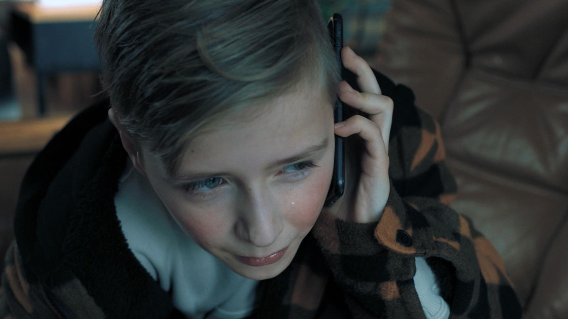 Nachgestellte Szene: Ein kleiner Junge hält sich weinend ein Smartphone an sein Ohr.