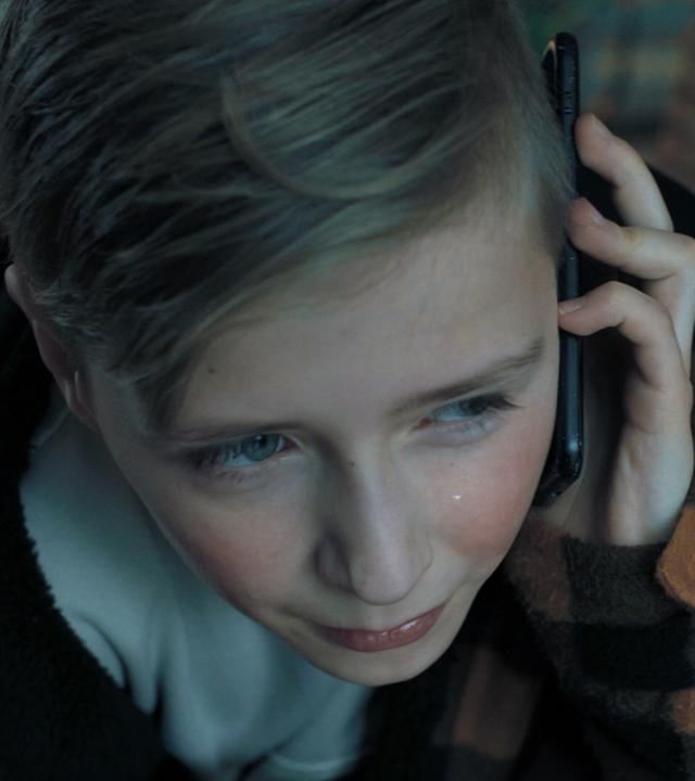 Nachgestellte Szene: Ein kleiner Junge hält sich weinend ein Smartphone an sein Ohr.