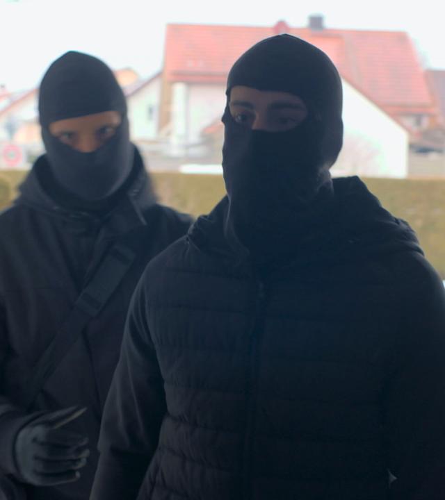 Nachgestellte Szene: Als eine Frau die Tür öffnet, steht sie zwei maskierten Männern gegenüber.