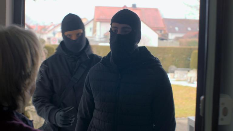 Nachgestellte Szene: Als eine Frau die Tür öffnet, steht sie zwei maskierten Männern gegenüber.