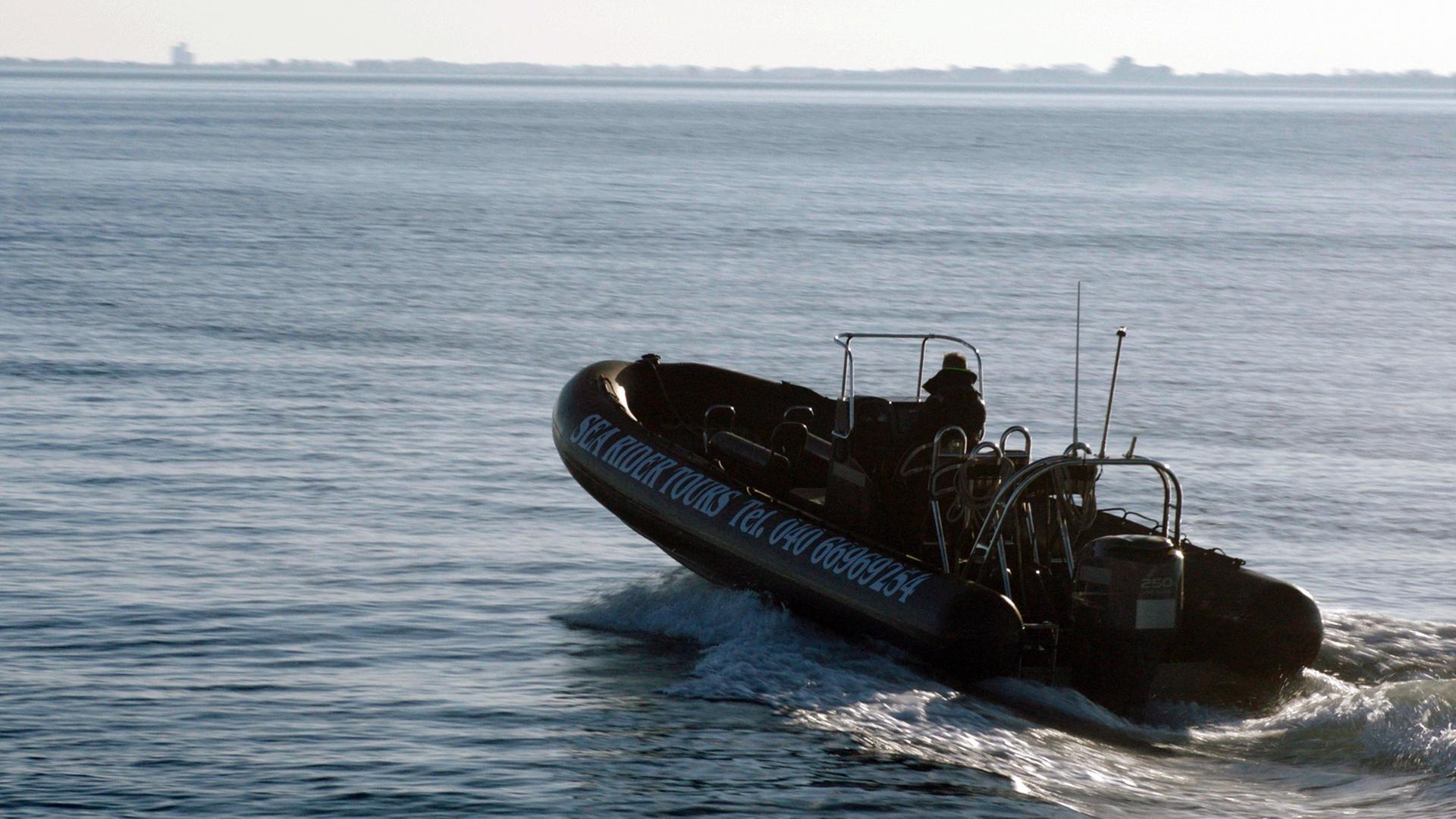 Nachgestellte Szene: Ein Schlauchboot mit Außenbordmotor und einem Mann am Steuerrad fährt Richtung offener See.