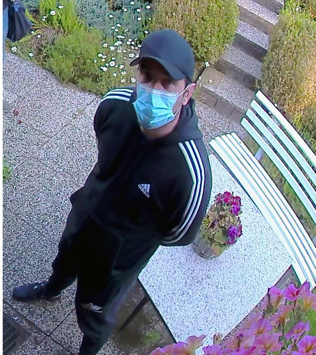 Die Gesuchten warten vor der Tür. Links ein Mann mit schwarzer Kappe, blauem Mundschutz, schwarzem Longsleeve und Jeans, sowie Gummihandschuhen. Rechts ein Mann mit schwarzer Kappe, schwarzem Adidas-Anzug mit weißen Streifen und hellblauem Mundschutz.