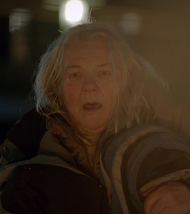 Nachgestellte Szene: Eine ältere, obdachlose Frau flüchtet aus ihrem brennenden Zeltlager.