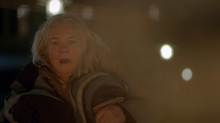 Nachgestellte Szene: Eine ältere, obdachlose Frau flüchtet aus ihrem brennenden Zeltlager.