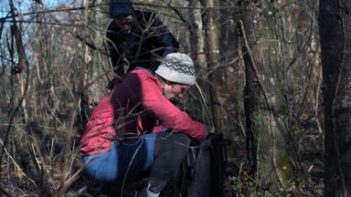 Nachgestellte Szene: Ein junger Mann hockt zwischen Bäumen und durchsucht den Inhalt eines Rucksacks.