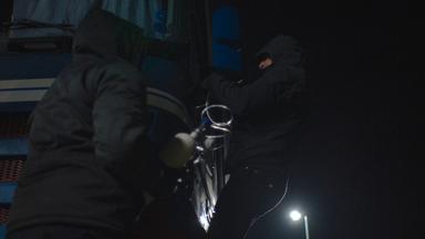 Nachgestellte Szene: Zwei schwarz gekleidete Männer leiten Gas in die Kabine eines LKWs.