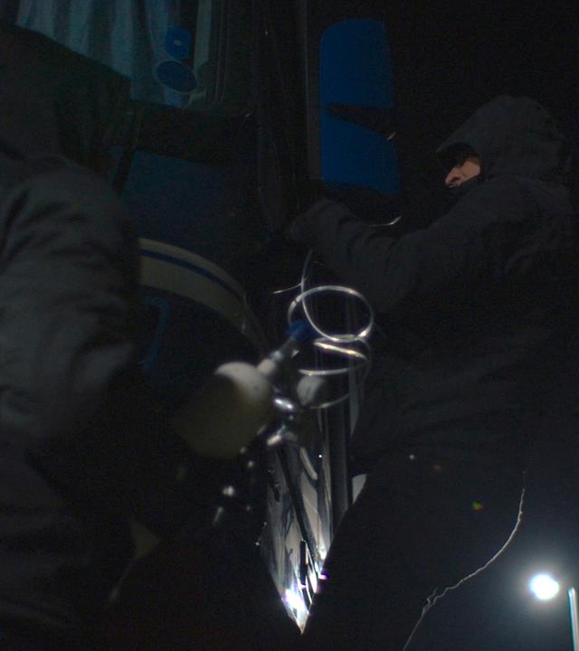 Nachgestellte Szene: Zwei schwarz gekleidete Männer leiten Gas in die Kabine eines LKWs.