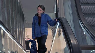 Nachgestellte Szene: Ein Mädchen auf einer Rolltreppe mit einer Einkaufstüte in der Hand.