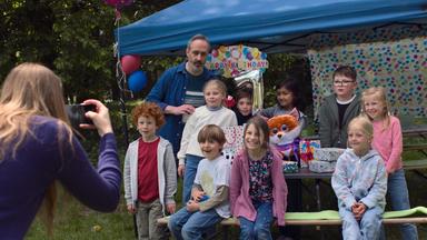 Nachgestellte Szene: Kinder bei einer Geburtstagsfeier, die lachend fotografiert werden.