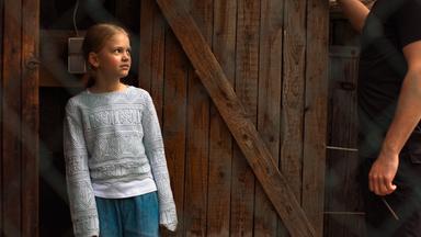 Nachgestellte Szene: Ein siebenjähriges Mädchen schaut ängstlich zu einem Mann. Sie steht in der Tür eines Holzunterstandes.