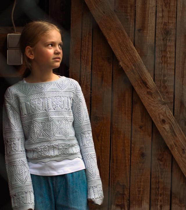 Nachgestellte Szene: Ein siebenjähriges Mädchen schaut ängstlich zu einem Mann. Sie steht in der Tür eines Holzunterstandes.