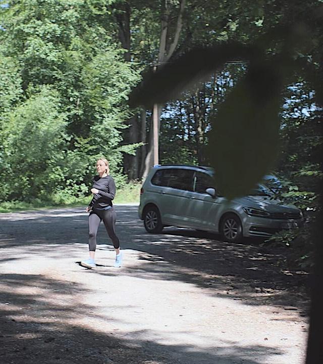 Nachgestellte Szene: Eine Frau in Sportkleidung joggt auf einem Parkplatz im Wald.