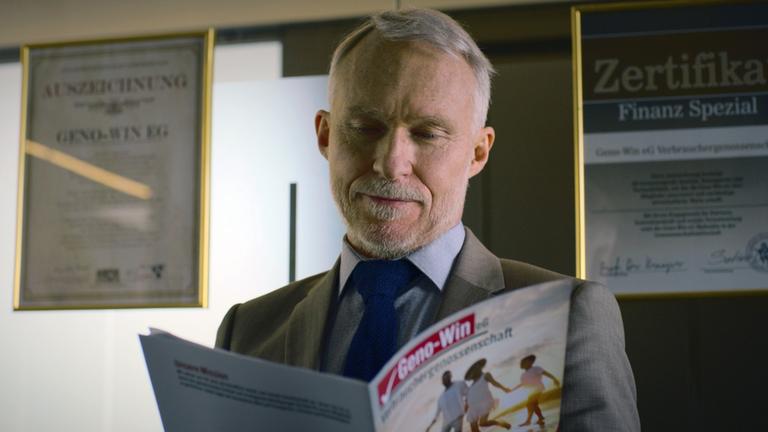 XY-Szenenfoto: Ein älterer Mann informiert sich in einer Fachbroschüre über Genossenschaftsinvestitionen im Ausland.