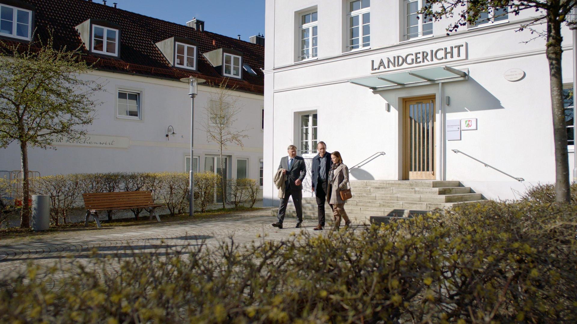 XY-Szenenfoto: Eine Frau und zwei Männer verlassen ein Gerichtsgebäude. 