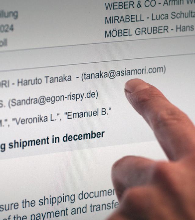 XY-Szenenfoto: Ein Zeigefinger weist auf einem Computerbildschirm auf die Absender-Adresse einer E-Mail.