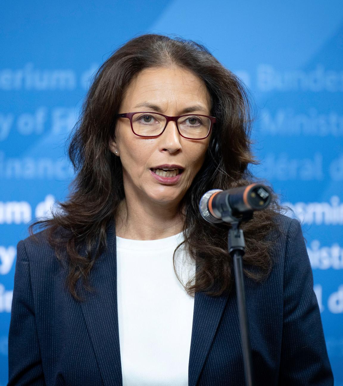 Yasmin Fahimi spricht vor einer blauen Wand im Finanzministerium in ein Mikrofon.