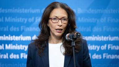 Yasmin Fahimi spricht vor einer blauen Wand im Finanzministerium in ein Mikrofon.