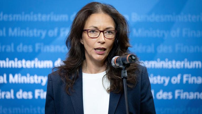 Yasmin Fahimi spricht vor einer blauen Wand im Finanzministerium in ein Mikrofon.