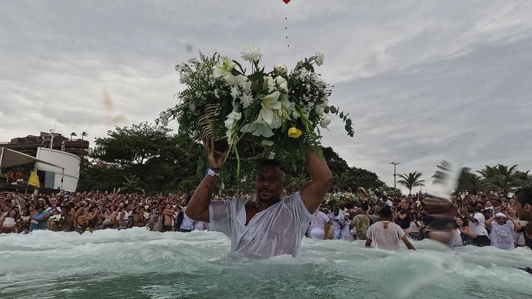 Ein Mann hält einen traditionellen Blumenkorb auf dem Kopf und trägt in ins Meer