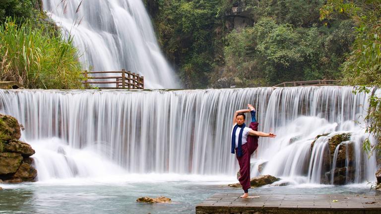 Mann praktiziert Yoga vor einem Wasserfall