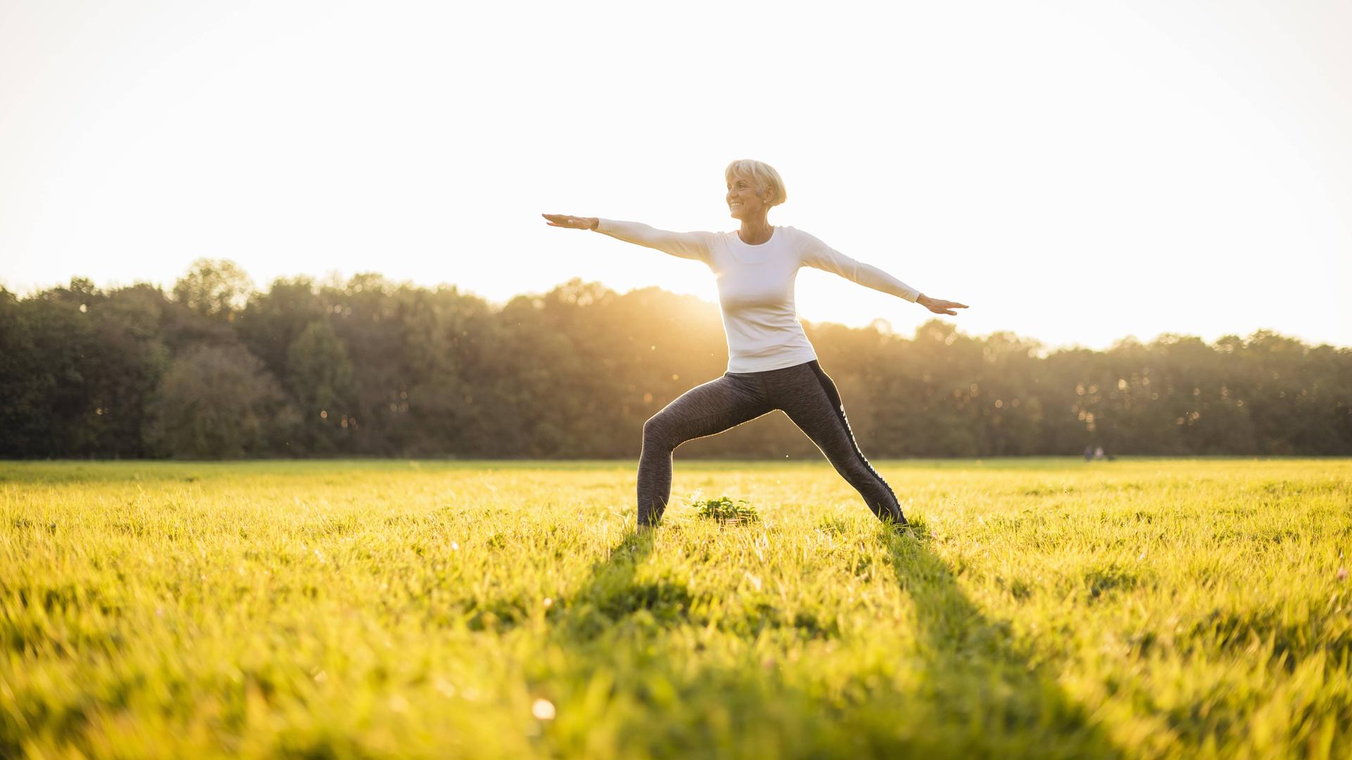 Frau macht Yoga auf einer Wiese.