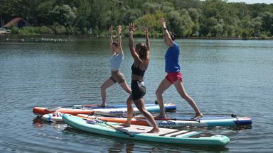 Personen stehen auf dem SUP im Wasser und machen Yoga