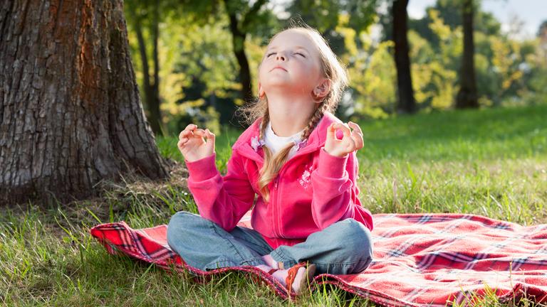 Mädchen sitzt in Yoga-Pose auf einer Decke im Park.