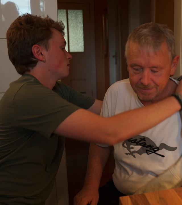 Young Carer Elmo zieht seinem pflegebedürftigen Vater eine Jacke über.