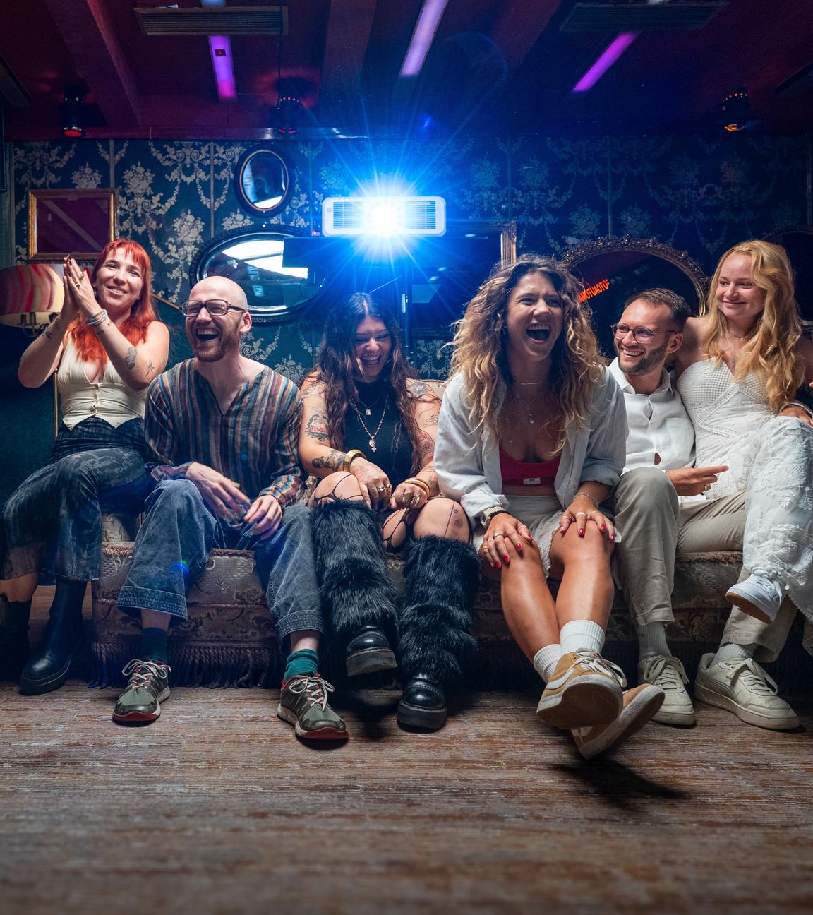 Janine "Nine", Emmanuel "Emma", Defne, Yasmin "Yaz", Nico und Josephine "Jo" sitzen auf einem Sofa und lachen in die Kamera.