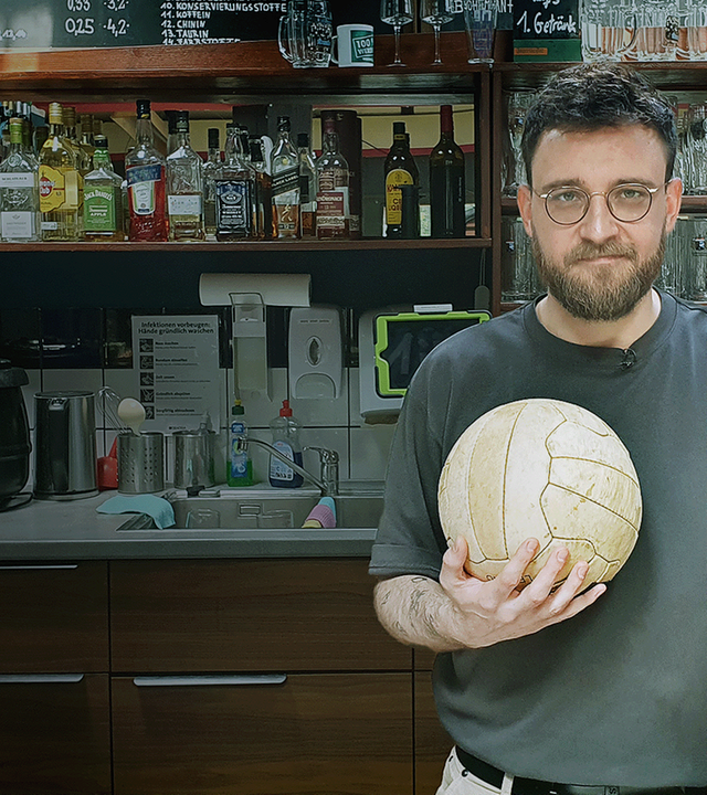 Nico Heymer mit Fußball und Bier in der Hand hinter Kneipentresen