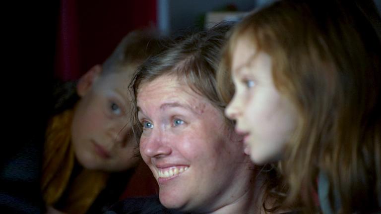 Frau, lächelnd schaut in der Mitte auf Bildschirm, rechts und links daneben schauen mit.