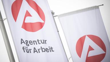 Fahnen mit dem Logo der Agentur für Arbeit wehen im Wind. 