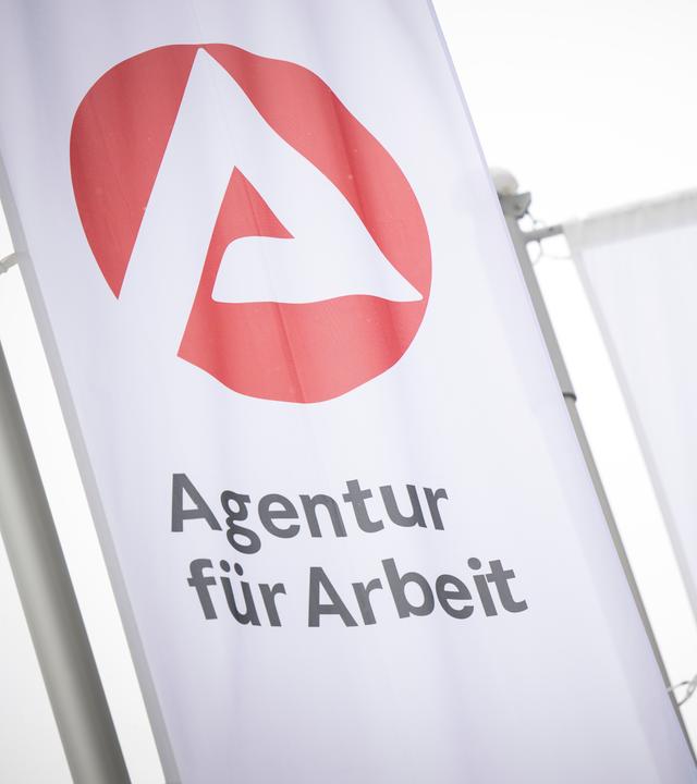 Fahnen mit dem Logo der Agentur für Arbeit wehen im Wind. 