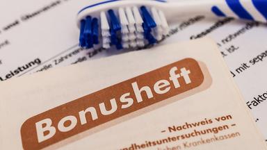 Ein Zahnarzt-Bonusheft, eine Zahnarztrechnung und eine blau weiße Handzahnbürste