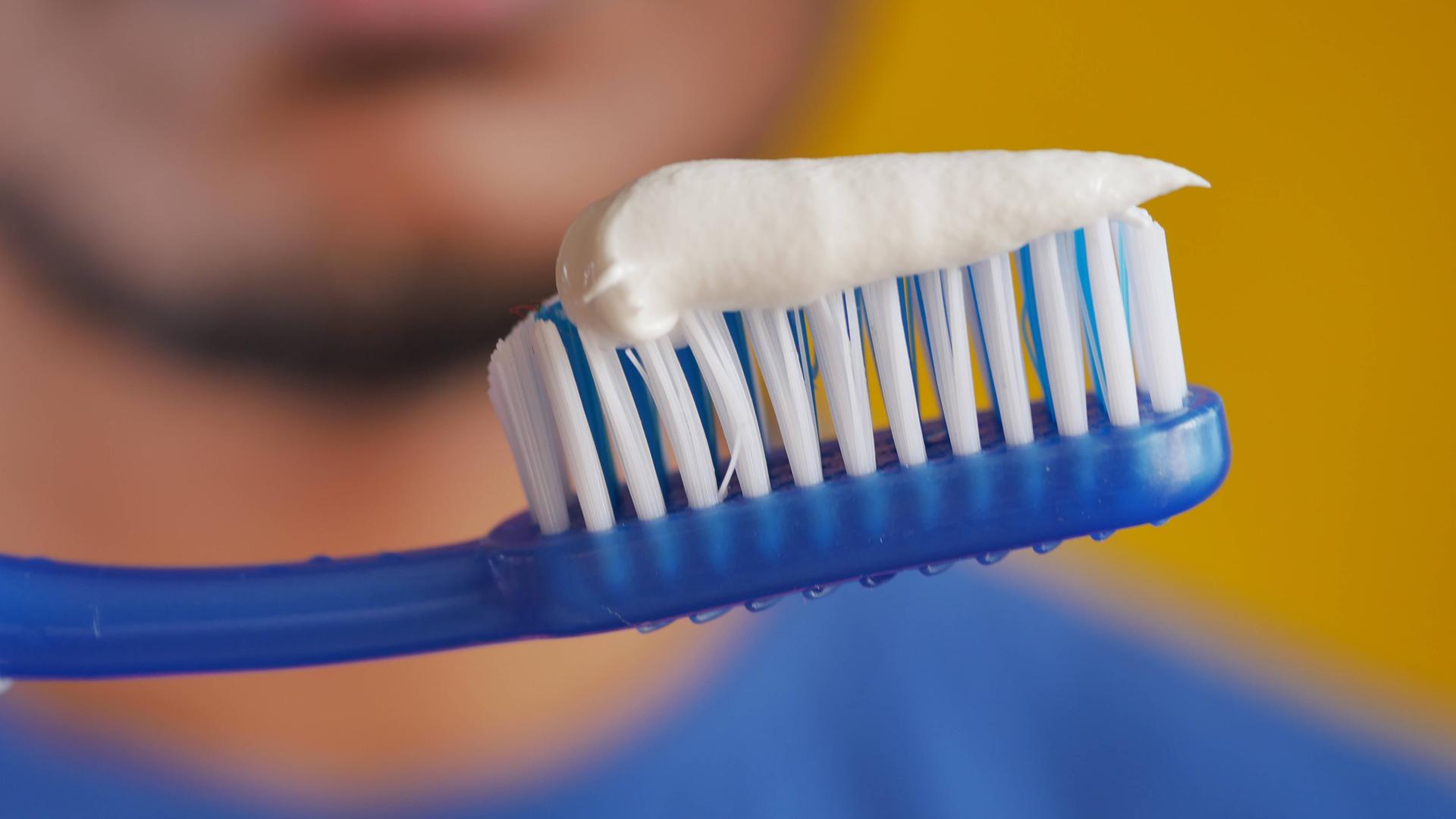 Ein Mann hält eine Zahnbürste, auf die Zahnpasta aufgetragen wurde.