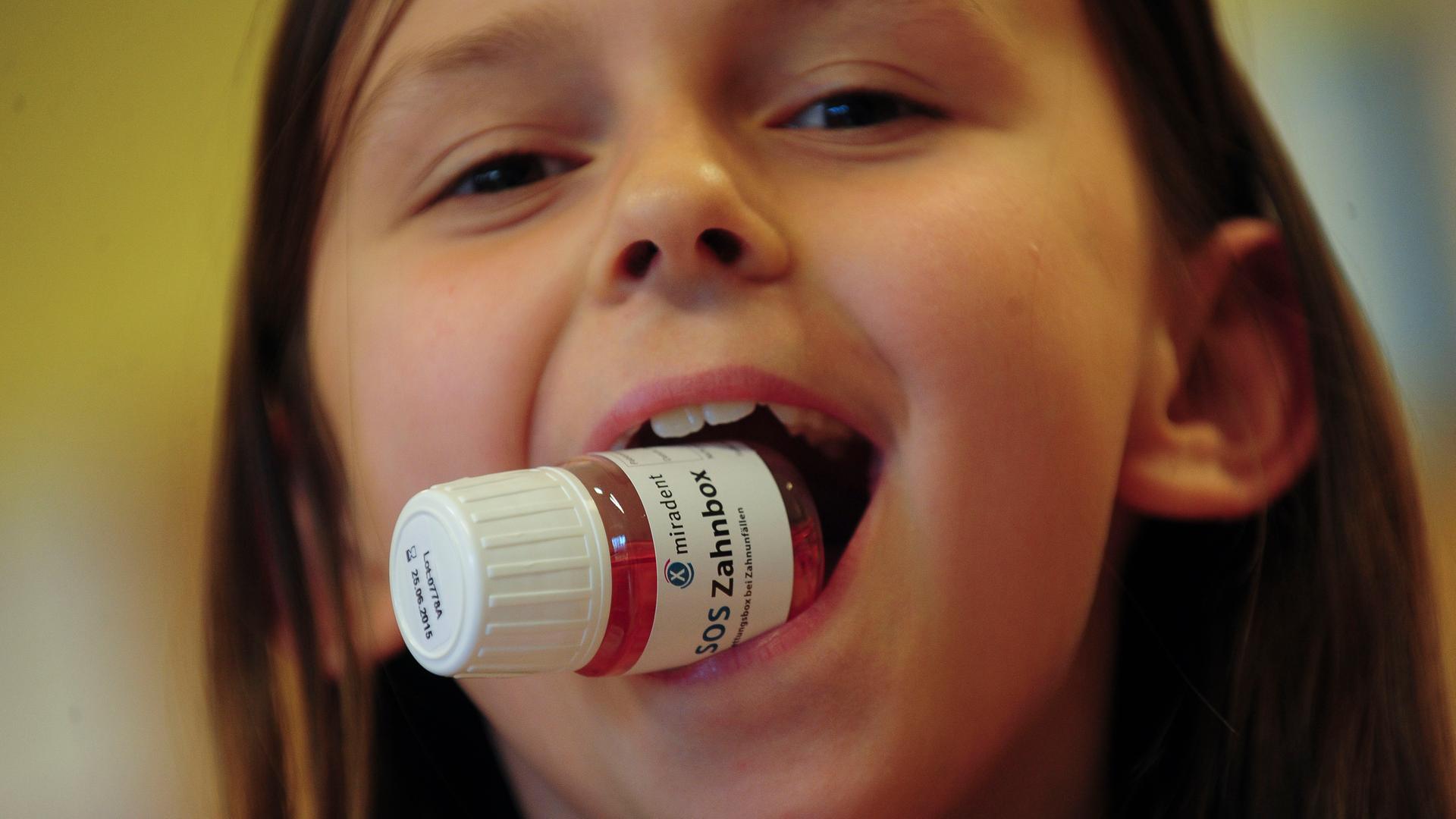  Kind lächelt mit einer Zahnrettungsbox im Mund