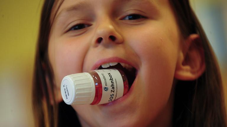  Kind lächelt mit einer Zahnrettungsbox im Mund