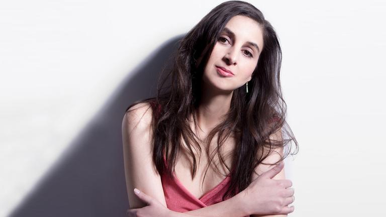 Dotschy Reinhardt, steht frontal zur Kamera und lächelt. Sie trägt ein rotes, ärmelloses Kleid