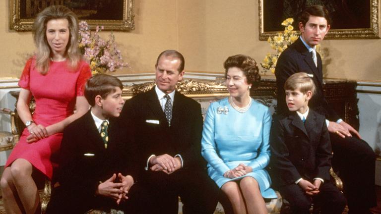 Die britische Königsfamilie rund um Queen Elizabeth II. ist auf dem Bild zu sehen. Charles und Anne auf den Armlehnen der Couch, Andrew und Edward neben ihren Eltern Philip und Elizabeth.