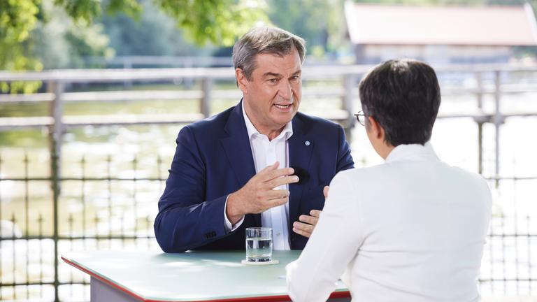 "Berlin direkt - Sommerinterview": Markus Söder und Shakuntala Banerjee sitzen sich zum Gespräch an einem Tisch gegenüber.