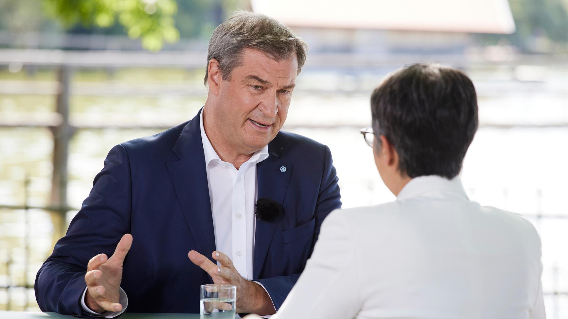 "Berlin direkt - Sommerinterview": Markus Söder und Shakuntala Banerjee sitzen sich zum Gespräch an einem Tisch gegenüber.