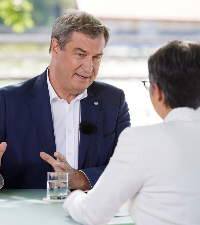 "Berlin direkt - Sommerinterview": Markus Söder und Shakuntala Banerjee sitzen sich zum Gespräch an einem Tisch gegenüber.